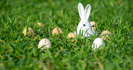 Fototapeta na wymiar white ceramic rabbit on green grass in a field with eggs