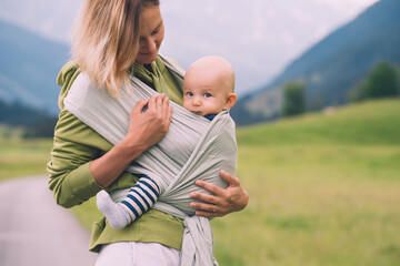 Babywearing. Mother and baby on nature outdoors. Baby in wrap carrier. Woman carrying little child in baby sling in green mint color. Concept of green parenting, natural motherhood, postpartum period.