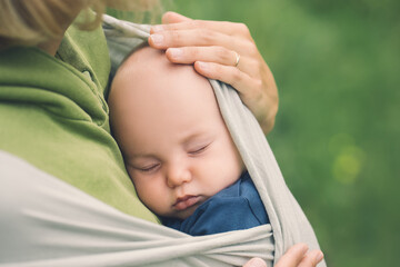 Babywearing. Mother and baby on nature outdoors. Baby in wrap carrier. Woman carrying little child...