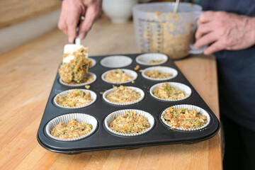 Hands of a man filling vegetable dough in a muffin baking tray for healthy savory cupcakes, vegetarian and vegan low carb diet, selected focus