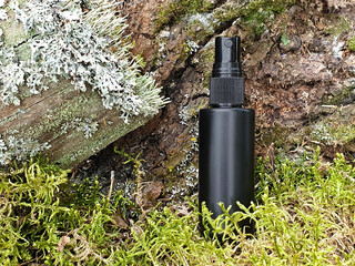 Unbranded black plastic spray and green forest moss, noisy background. Front view, mockup. Cosmetic bottle container for branding. Deodorant for feet and shoes.