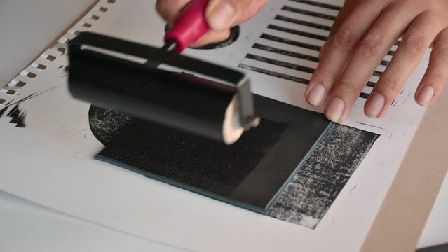 Woman using brayer roller with black ink for lino print