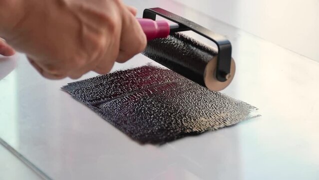 Woman using brayer roller with black ink for lino print