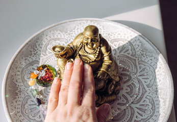 Person hand rubbing small golden laughing Buddha figurine tummy. It believed to bring happiness, good fortune and wealth. Buddai monk.