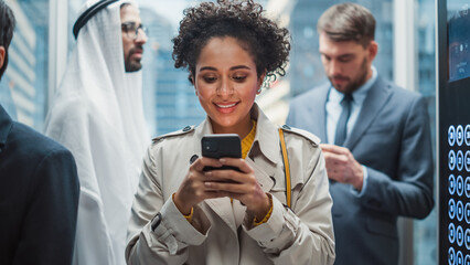 Four Diverse Multiethnic International People Ride a Glass Elevator to Office in a Modern Business Center. Focus on Young Stylish Black Latin Businesswoman Using Smartphone in a Lift.
