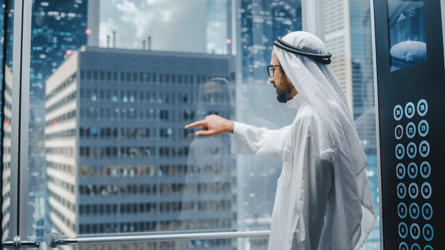Successful Muslim Businessman in Traditional White Kandura Riding Glass Elevator to Office in Modern Business Center. Arab Male Interacting With Mock Up Holographic Screen in the Lift Concept.