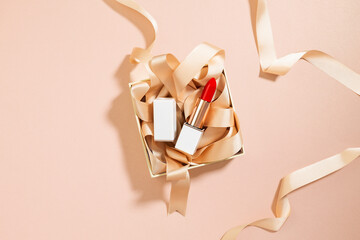 red lipstick and ribbon in gift box on pink background