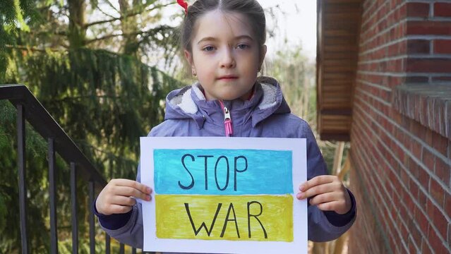 Ukrainian poor toddler girl kid homeless protesting armored conflict holding banner with inscription message text Stop War on background of yellow blue flag. Crisis, peace, stop aggression in whole
