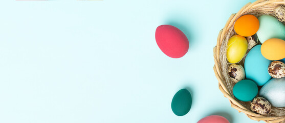 Colorful Easter eggs lie in a basket on a blue background. Easter holiday concept, flat lay. Banner.