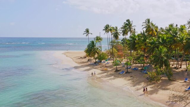 Aerial view showing tourist resting on tropical sandy beach with clear Caribbean Sea and Palm trees in background - Beautiful sunny day at Playa Punta Popy,Dominican Republic