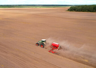Obraz premium Tractor plowing farm field, sowing seed on plowed field. Spring planting season. Tractor with disk harrow on plowing field. Farming seeding. Seed sowing and land cultivating. Tractor Plowing field..