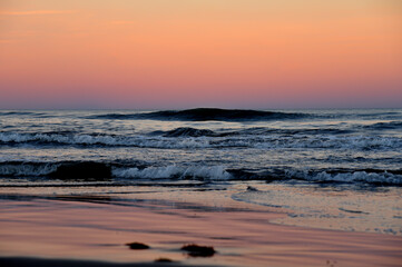 Waves in sea on sunset background. Waves in sea during storm and wind. Wave from the sea goes on land to the beach. Splashing Waves in ocean, background, texture. Wave at Rising Storm. Seashore.