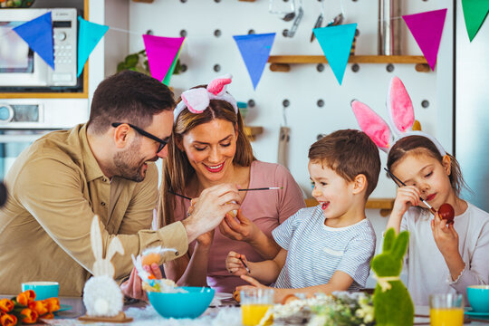 Family painting Easter eggs together at table. Laughing family on Easter. Happy young family with two children painting Easter eggs at home. Easter. Happy family