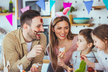 Lovely family prepare for Easter at domestic kitchen. Mother, father, son and daughters are painting eggs. Happy family are preparing for Easter. Cute little child girl and boy wearing bunny ears.