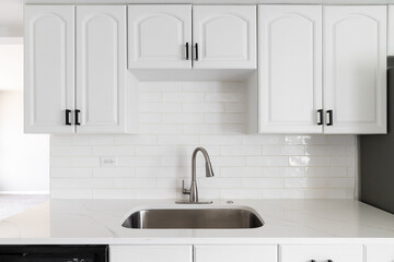 A kitchen with white cabinets, subway tiles, and marble countertop.
