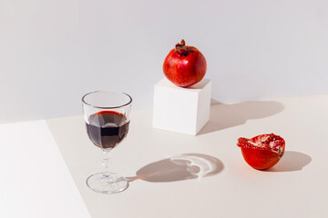 Creative composition made of glass of red wine or juice and pomegranates on pastel backgound with sunlit. Summer refreshment concept. Minimal style.