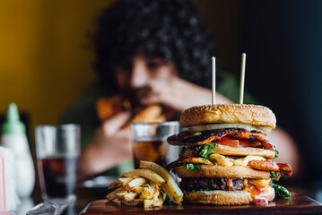 Close-up of a delicious, large hamburger and a child in the background eating it. 