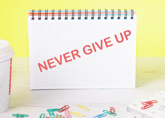 Never give up text on a notebook standing on a table on a yellow background