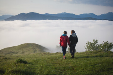 Fototapeta na wymiar Young Couple Walks Holding Hands in Amazing Carpathian Misty Mountain Scenery