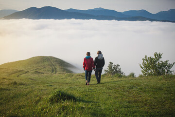 Fototapeta na wymiar Young Couple Walks Holding Hands in Amazing Carpathian Misty Mountain Scenery