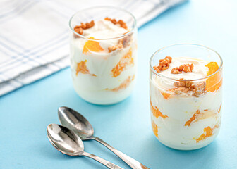 Greek yogurt with orange and walnuts in glasses on a blue table. Healthy food. Health eating concept. Selective focus.