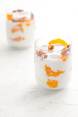 Greek yogurt with orange and walnuts in glasses on a white table. Healthy food. Health eating concept. Selective focus.
