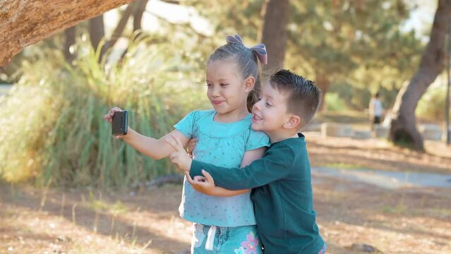 Ni&ntilde;os felices tom&aacute;ndose fotos fotograf&iacute;as selfies retrato con el celular jugando y disfrutando en el parque abrazados al aire libre en tronco caf&eacute; de un &aacute;rbol