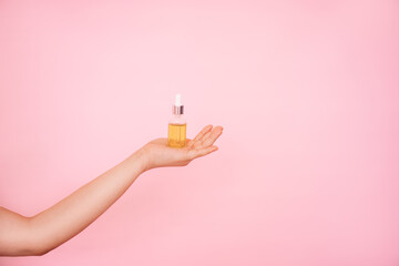 A transparent dropper bottle with serum, lotion or essential oil in a woman's hand on a pink background. The concept of cosmetics for skin care.