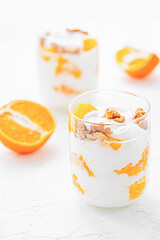 Greek yogurt with orange and walnuts in glasses on a white table. Healthy food. Health eating concept. Selective focus.