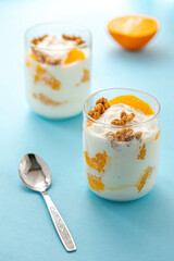 Greek yogurt with orange and walnuts in glasses on a blue table. Healthy food. Health eating concept. Selective focus.