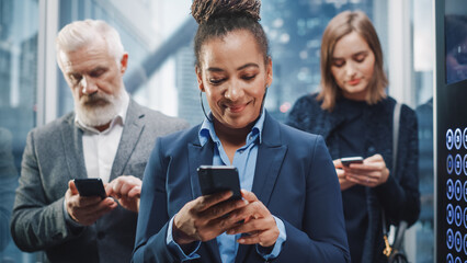 Three Diverse Multiethnic International People Ride a Glass Elevator to Office in a Modern Business Center. Focus on African American Businesswoman Using Smartphone in a Lift.