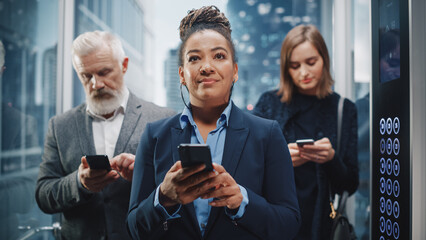 Three Diverse Multiethnic International People Ride a Glass Elevator to Office in a Modern Business Center. Focus on African American Businesswoman Using Smartphone in a Lift. © Gorodenkoff