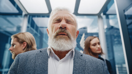 Fototapeta premium Close Up Portrait of a Middle Aged Man Sneezing in a Crowded Glass Elevator in a Modern Office Building. Businessman Covers His Face, but Other People Are Afraid to Catch the Virus in a Lift.