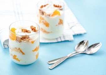 Greek yogurt with orange and walnuts in glasses on a blue table. Healthy food. Health eating concept. Selective focus.