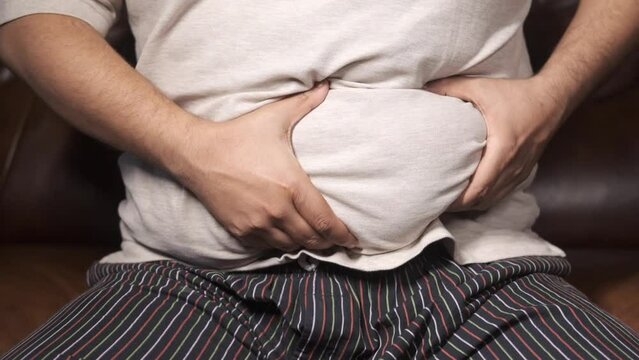 man's hand holding excessive belly fat, overweight concept