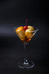 Neapolitan Rum baba (or baba au rum) in a martini glass with a cocktail cherry on a black background. Small yeast cakes soaked in rum syrup. Traditional Italian pastry. Close-up, selective focus.