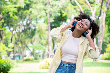 Smiling charming African American woman in imagined dreaming while listening favorite songs during the leisure on the sunny meadow at park.