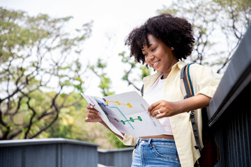 Charming African woman holding poster map traveling to natural attractions and the public park. Journey of travel and environment studies.