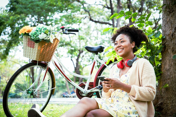 Smiling charming African American woman in imagined dreaming after communication and listening favorite songs with headphones during the picnic on the sunny meadow. Banner cover - obrazy, fototapety, plakaty