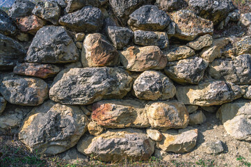 The background of the stones of the ancient wall. Dark stones left after the destruction of ancient buildings. Dark rock.