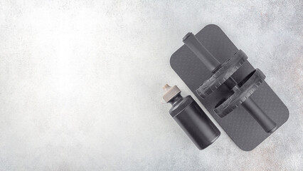 Black ab roller with mat, sport bottle of water on a gray concrete background, top view, copy space. Home workout. Fitness and activity. 