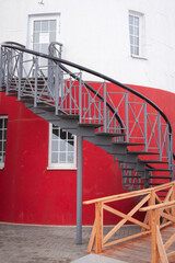 A full frame of a spiral stairs going up towards the entrance of the red and white striped lighthouse