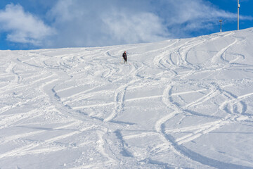 Fototapeta na wymiar Woman with brown hair, wearing ski wear and a bagpack skiing down a beautiful snow hill with plenty of tracks on the snow, view from the side from far away, stryn norway, horizontal