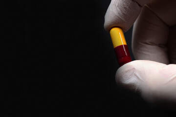 Doctor's hand with a capsule, antibiotic, or medicine pill on a black background for copy space