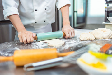 Smiling bakers looking at camera..Chef  baker in a chef dress and hat, cooking together in kitchen.Young asian man takes fresh baked cookies out of modern electric oven in kitchen.