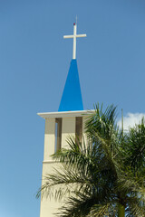 Topo de igreja com um crucifixo branco contra o céu azul. Igreja Nossa Senhora de Aparecida em Goiânia.