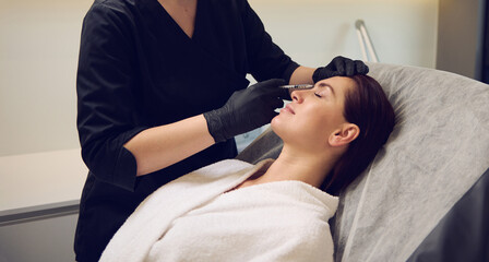 Beautician aesthetician injecting hyaluronic acid or botulinum toxin in the face of middle aged...