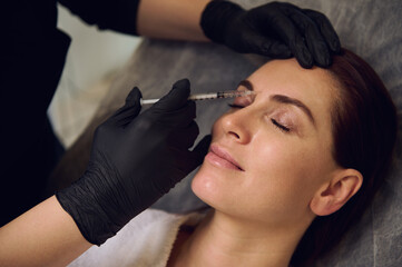 Close-up of beautiful middle aged woman getting beauty injections on her forehead in wellness spa cosmetology clinic. Botulinum toxin injection and hyaluronic acid for anti-wrinkle anti-aging therapy