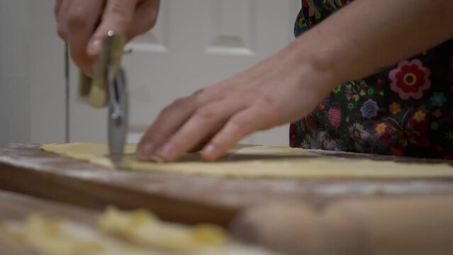 Woman Cutting Thin Dough Of Angels WIngs With Pizza Cutter On A Chopping Board. - close up
