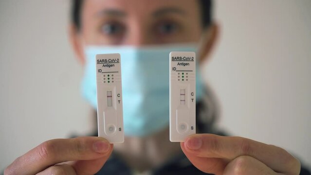 Woman in medical protective mask shows fast antigen test cassettes with reagents for detect coronavirus infection with positive and negative results. Stop COVID-19 infection and pandemic concept